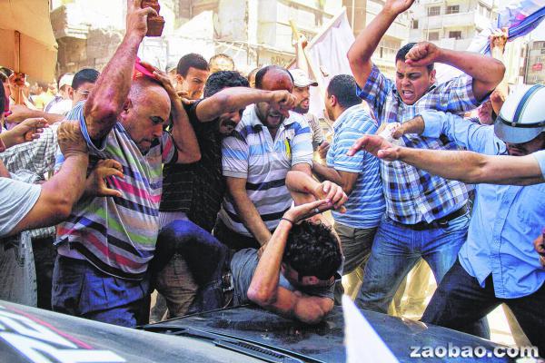 一名反对派支持者被大批总统穆尔西的支持者围殴，其中一名袭击者甚至用砖块来攻击反对派支持者。（图片来源：美联社）