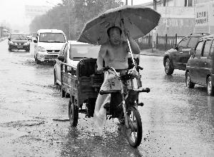 昨天，在王四营桥附近，一位骑三轮车的大爷打着伞在雨中前行。晨报记者 王巍/摄