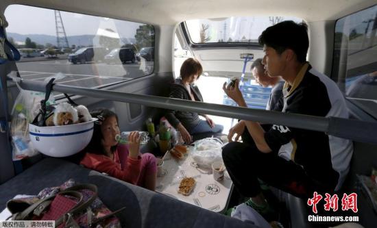 当地时间4月19日，日本熊本县益城町汇集众多地震避难者的停车场内，一家人在汽车内吃饭。