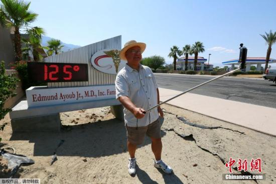 一名棕榈泉居民在显示高温的数字温度牌前举起自拍杆。当局称热浪“罕见而危险”，会有造成中暑等风险，呼吁民众避免长时间逗留室外。