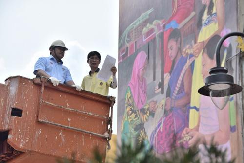 中国侨网蔡文涛向纳斯里（左）讲解巨型壁画的构图与含义。（马来西亚《星洲日报》）