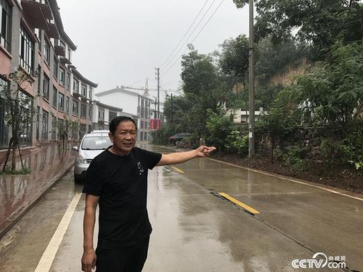 52岁赵书进手指着还没有开发的旧房子，在他身后是自己即将开业的商铺。（王莉莉 摄）